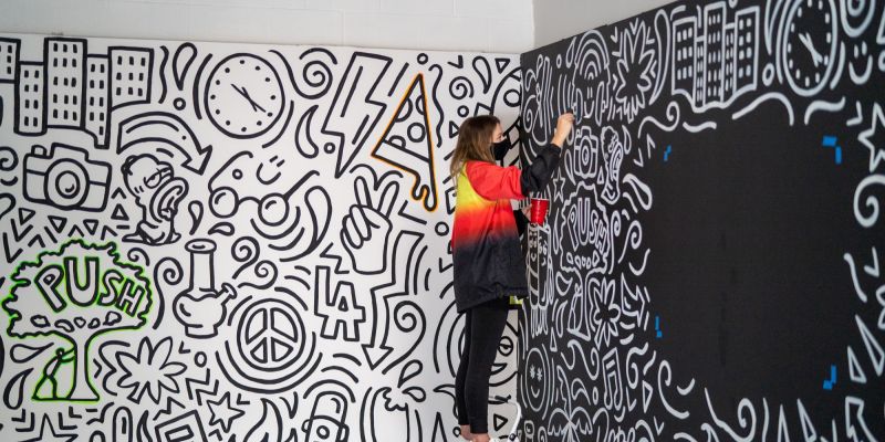 Malerin bei der Arbeit an einer bunten Wandgestaltung, repräsentiert die kreative Vielfalt und Fachexpertise, die in der Beratung für Künstler und Kreative angeboten wird.